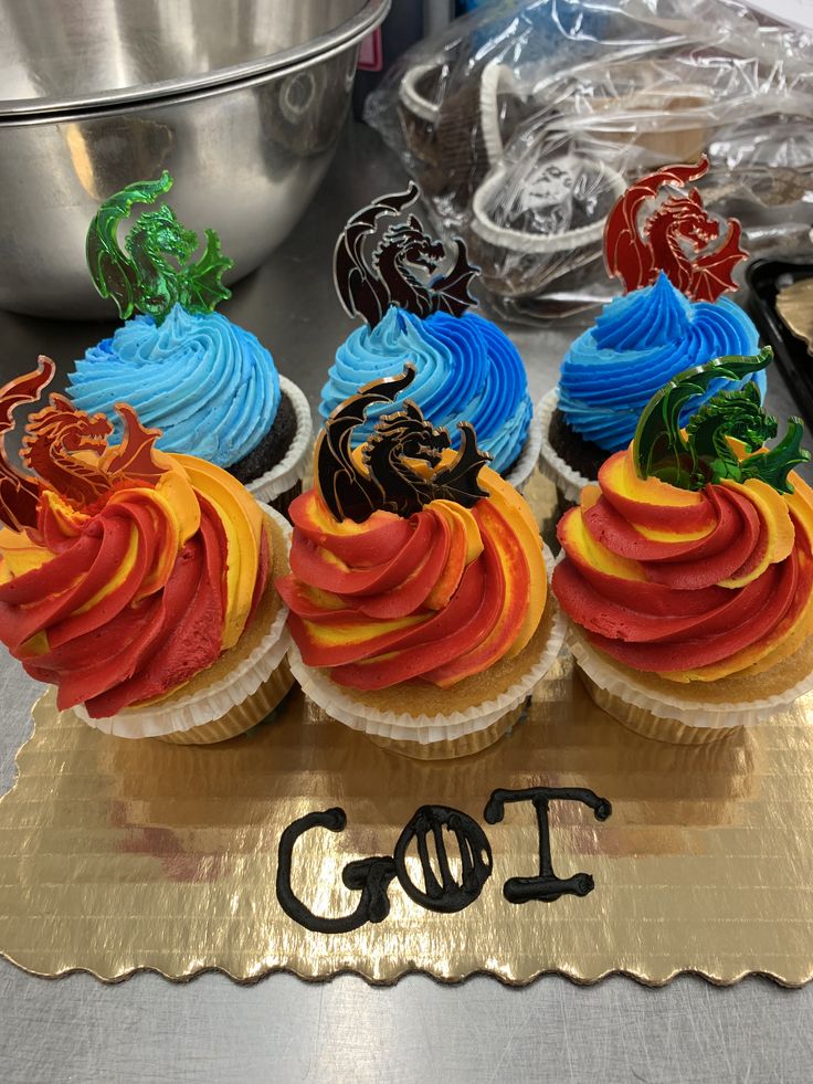 four cupcakes with colorful frosting sitting on top of a gold platter