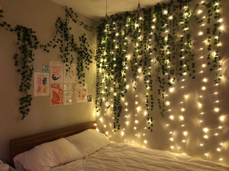 a bed with white sheets and lights hanging from the wall next to it's headboard