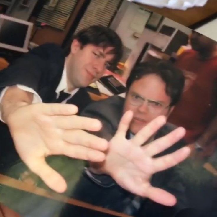 two men are sitting at a table with their hands in front of them and one man is holding out his hand