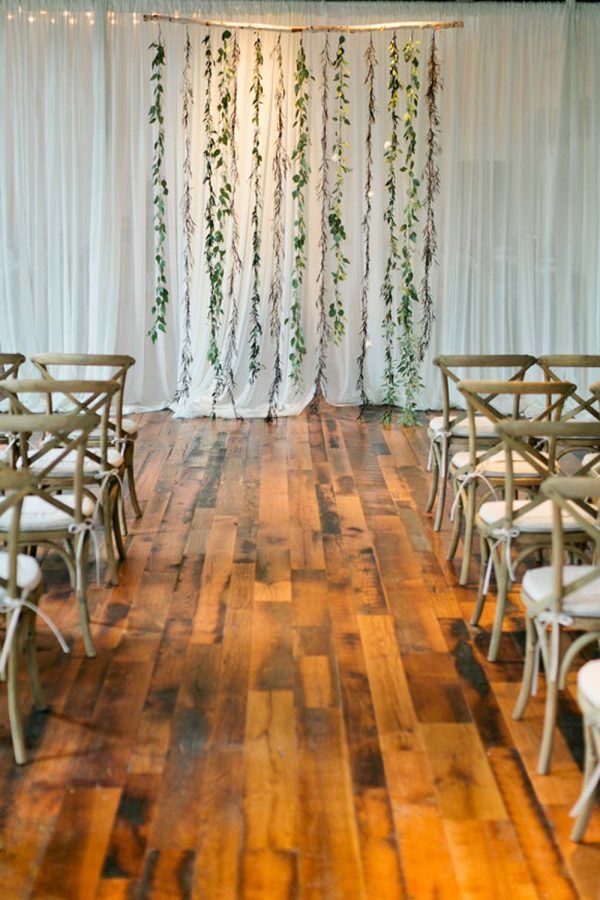 an indoor wedding ceremony with white drapes and greenery hanging from the back wall