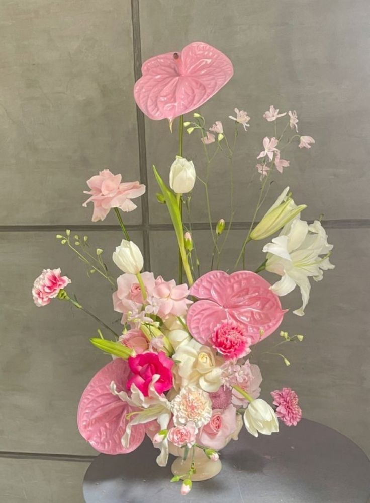 a vase filled with pink and white flowers on top of a metal table next to a wall