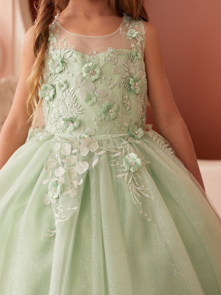 Step into a world of fairy-tale elegance with the Celine Glitter Tulle Girls Dress, a dazzling creation that's sure to make any little girl feel like royalty. The dress features an illusion neckline bodice that combines the magical allure of transparency with the security of full coverage, creating a sophisticated and modern silhouette. Adorning this ethereal bodice are delicate 3D flowers with beads, artfully placed to bring a garden of enchantment to life. The glitter tulle skirt is nothing sh Embellished Green Tulle Ball Gown, Green Embellished Tulle Ball Gown, Green Princess Dress With Floral Applique For Party, Fairytale Tulle Dress With Fitted Bodice, Embellished Green Ball Gown For Pageant, Embellished Green Ball Gown For Pageants, Green Princess Dress With Floral Applique, Princess Tulle Pageant Dress For Prom Season, Princess Style Pageant Dress With Floral Applique