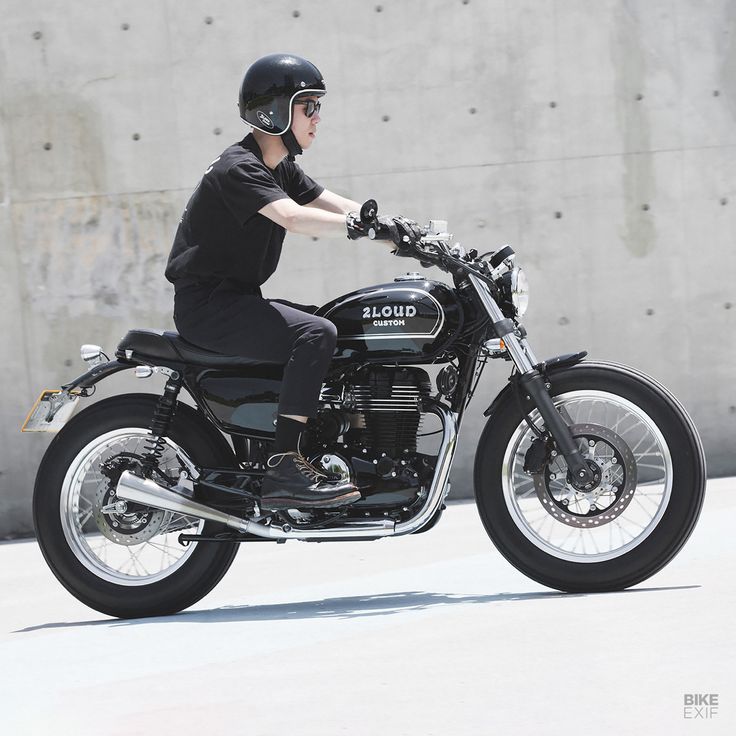 a man riding on the back of a motorcycle down a street next to a cement wall