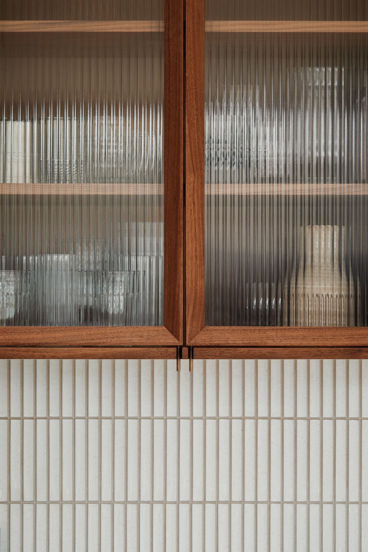 two wooden cabinets with glass doors on each side in front of a white tile backsplash