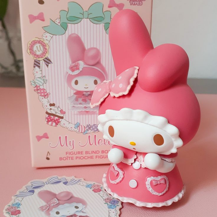 a hello kitty figurine next to a pink box and its packaging on a table