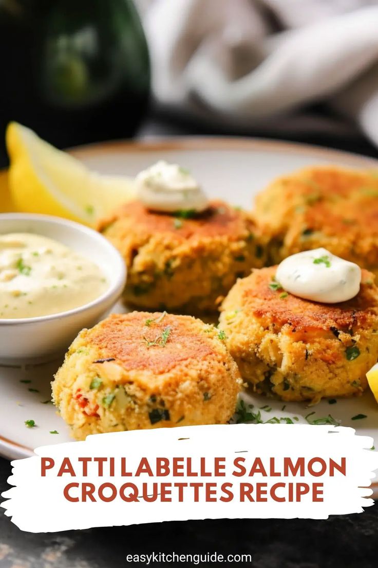 some crab cakes are on a plate with lemon wedges and cream sauce next to it