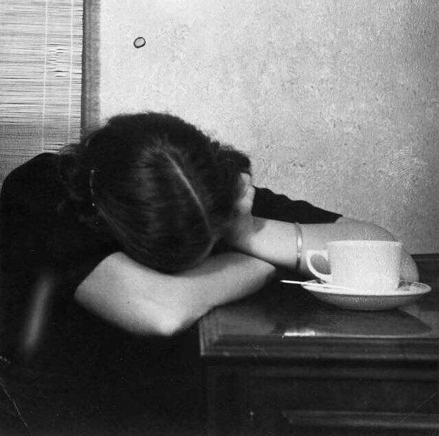 a woman sitting at a table with her head on a coffee cup and saucer