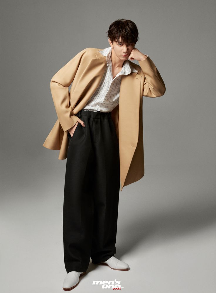 a young man is posing in black pants and a trench coat