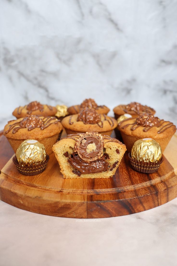 there are many cupcakes on the wooden platter with gold foiled decorations