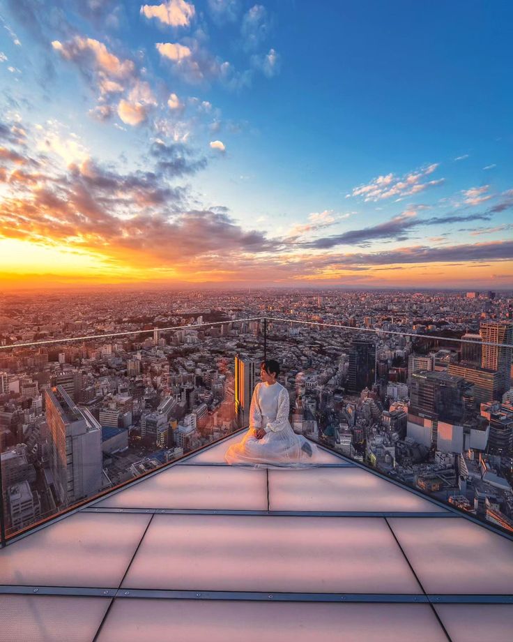 a person sitting on top of a building in the middle of a city at sunset