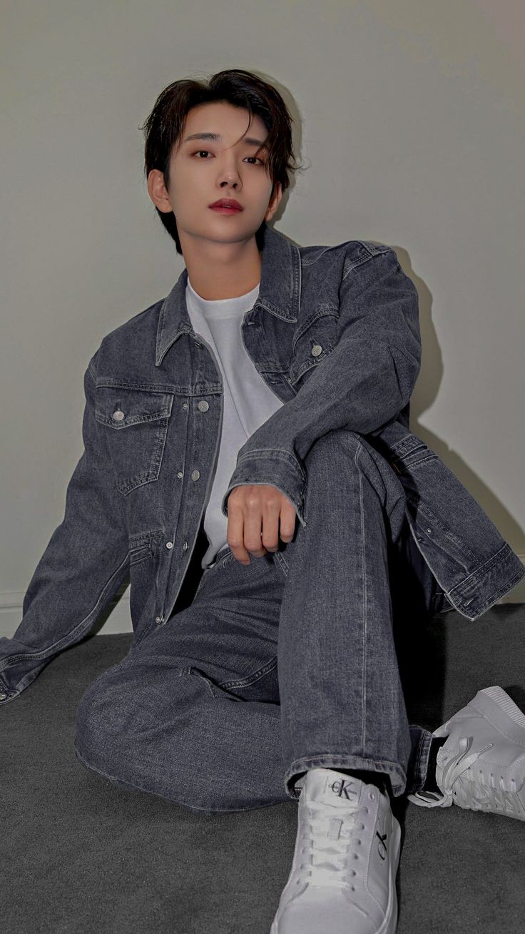 a young man sitting on the floor with his legs crossed wearing white sneakers and denim jacket