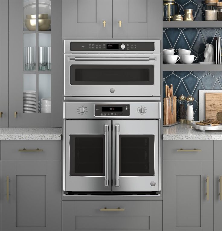 a stainless steel oven and microwave in a kitchen with gray cabinets, counter tops, and open shelving