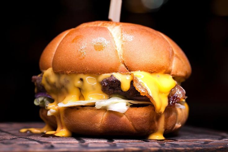 a cheeseburger with bacon and other toppings on a wooden table in front of a dark background