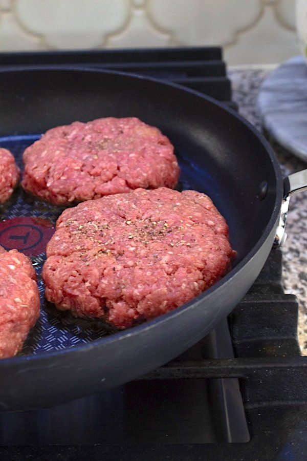 hamburger patties cooking in a frying pan on the stove top, ready to be cooked