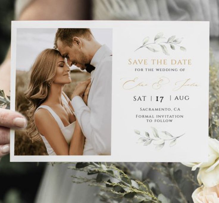 a person holding up a card that says save the date with flowers in front of them