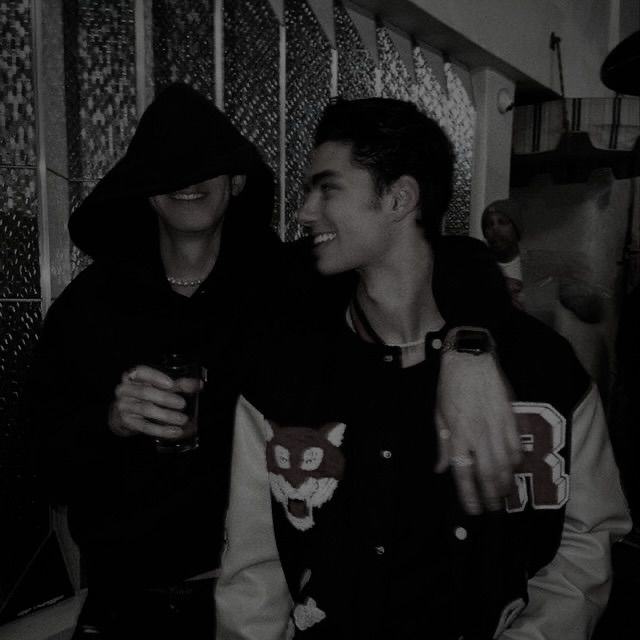 two young men standing next to each other in front of a staircase and one holding a drink