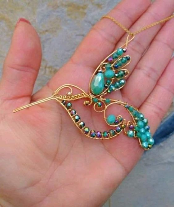 a hand holding a gold necklace with green beads and a butterfly shaped brooch on it