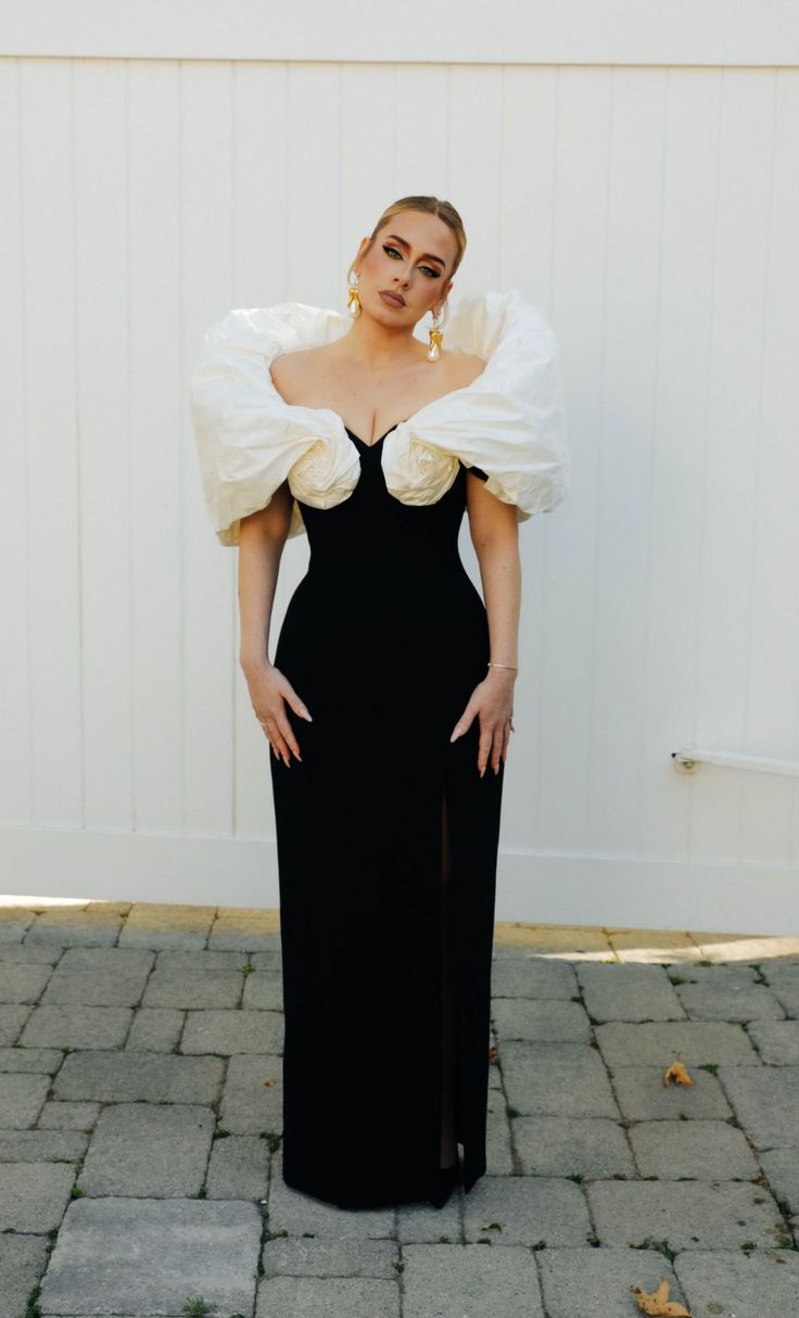 a woman standing in front of a white wall wearing a black dress with puff sleeves