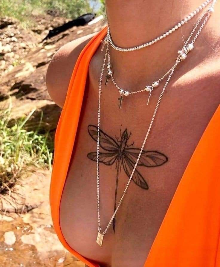 a woman's chest with a dragonfly tattoo on her chest and two necklaces attached to it