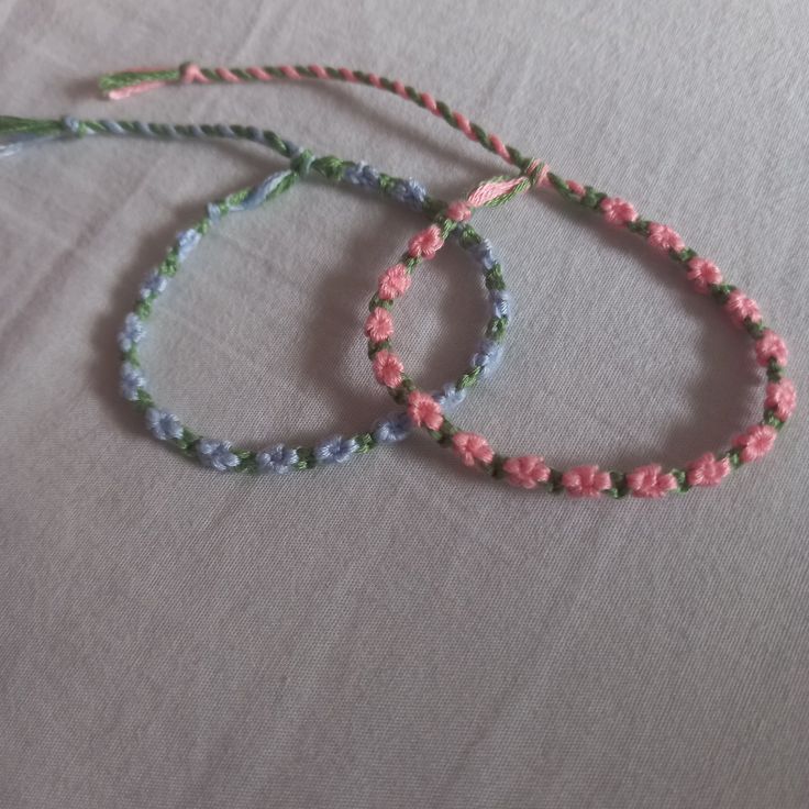 two bracelets made out of beads on top of a white table with pink and green flowers