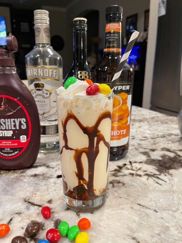 there is a drink on the counter with candy and liquor bottles in the back ground