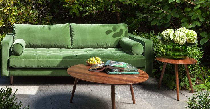 a green couch sitting next to a wooden table on top of a stone floor covered in greenery