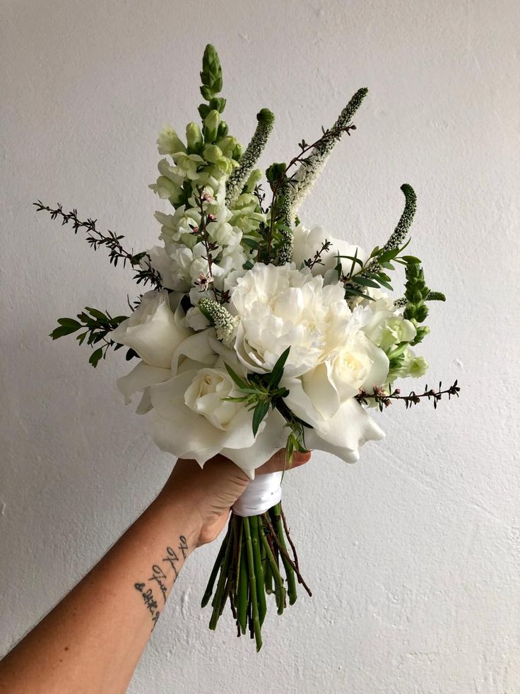 a person holding a bouquet of white flowers in their hand with tattoos on the arm