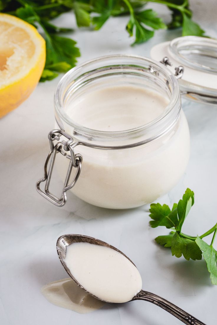 a glass jar filled with yogurt next to a lemon and some parsley