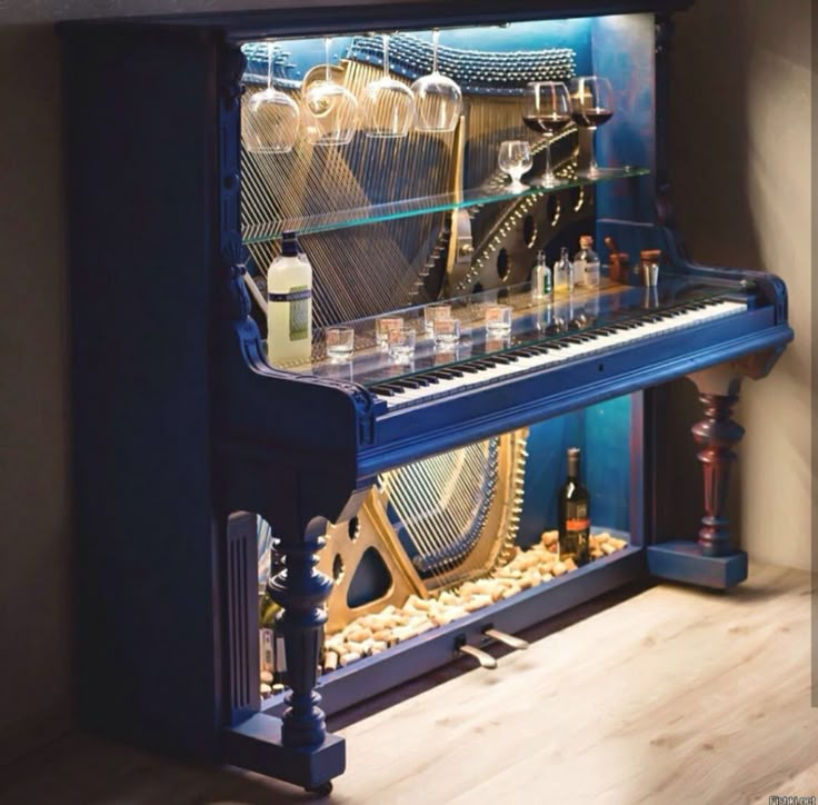 a blue piano sitting on top of a hard wood floor next to a shelf filled with wine glasses