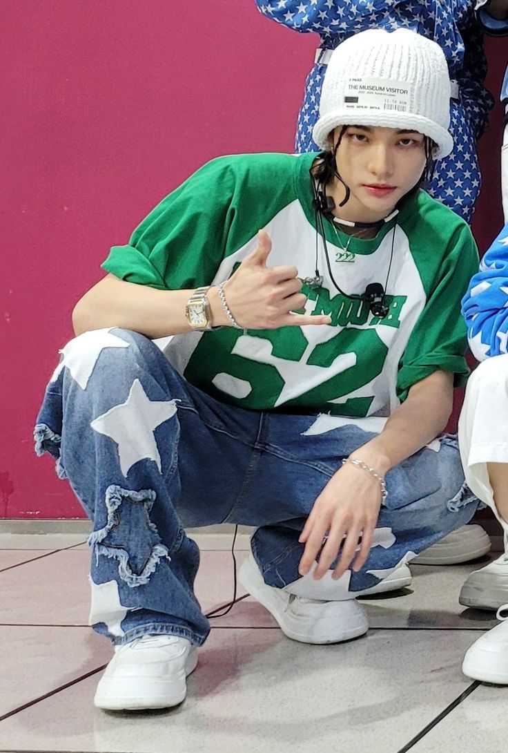 a young man sitting on the ground next to a teddy bear wearing a green and white shirt