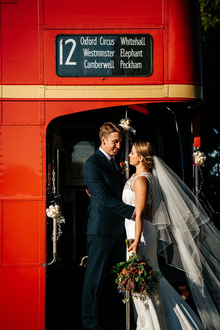 a bride and groom standing in front of a red double decker bus