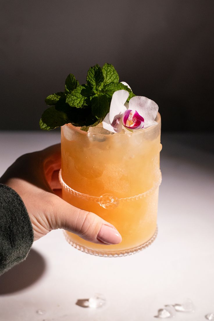 a hand holding a drink with a flower on it