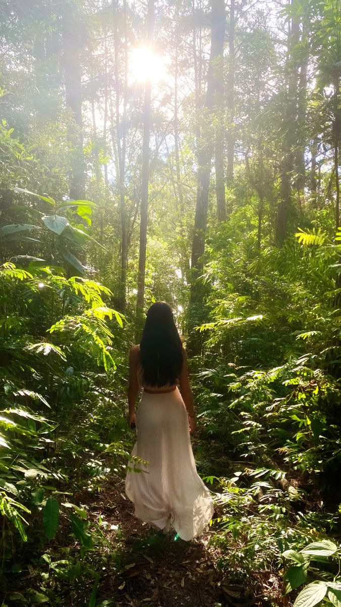 a woman is walking through the woods with her back turned to the camera and looking at the sun