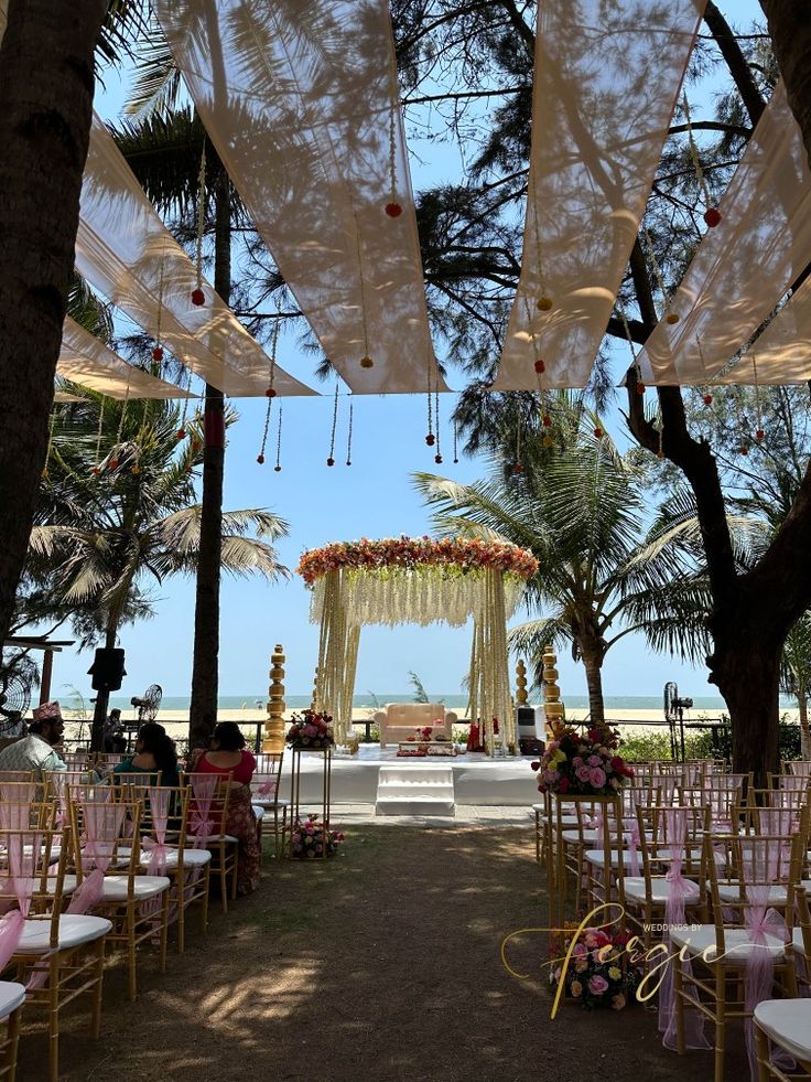 an outdoor ceremony set up with pink and white flowers on the aisle, surrounded by palm trees