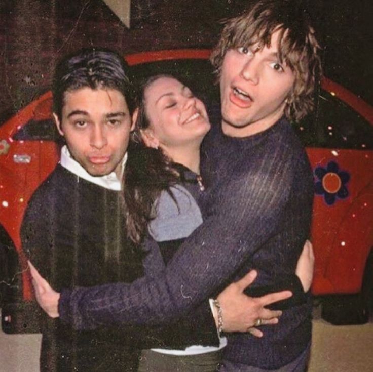 three people hugging each other in front of a red car