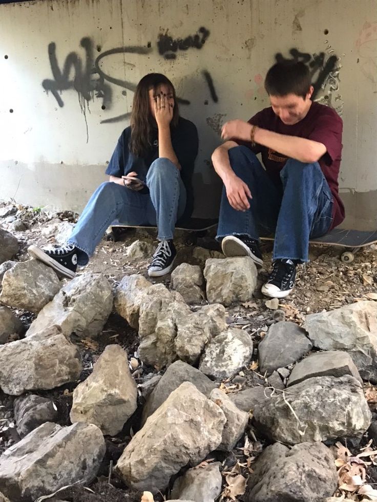 two people sitting on top of rocks in front of a wall with graffiti writing on it