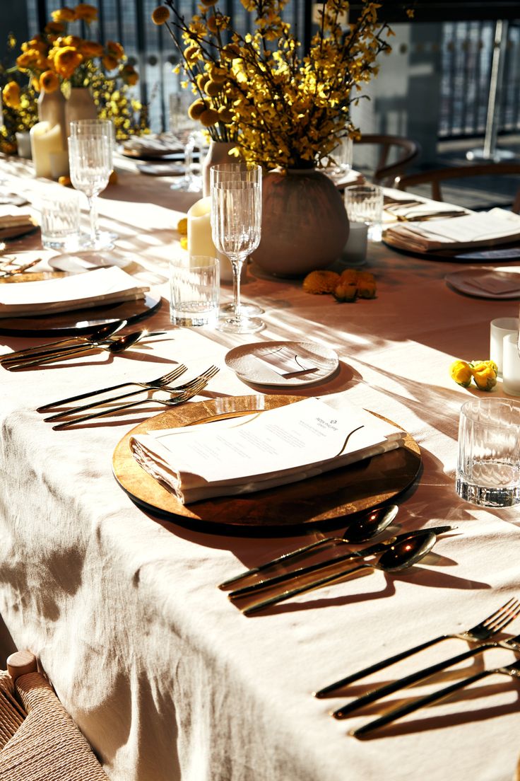 the table is set with silverware and yellow flowers