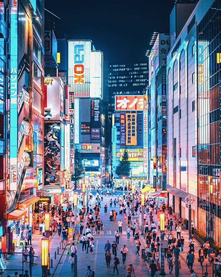 a city street filled with lots of people and tall buildings covered in neon colored lights