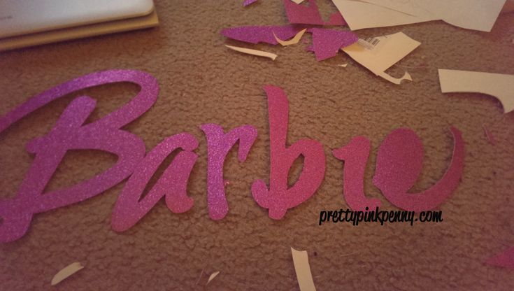 the word barbie is cut out of paper and placed on the floor next to a laptop