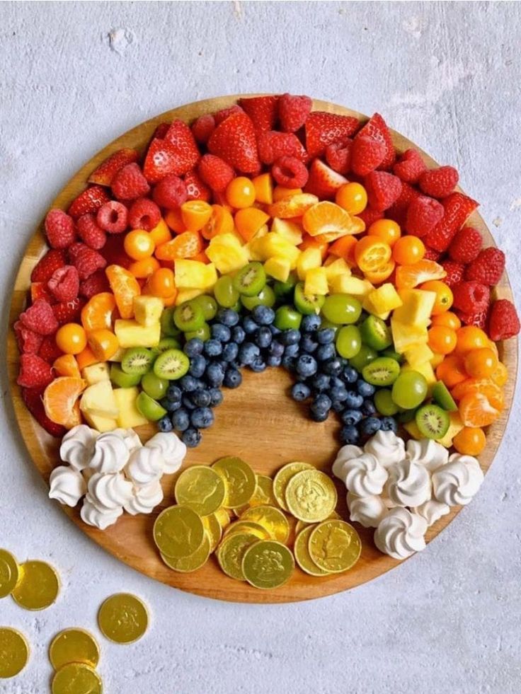 a wooden plate topped with lots of fruit and veggies next to gold coins