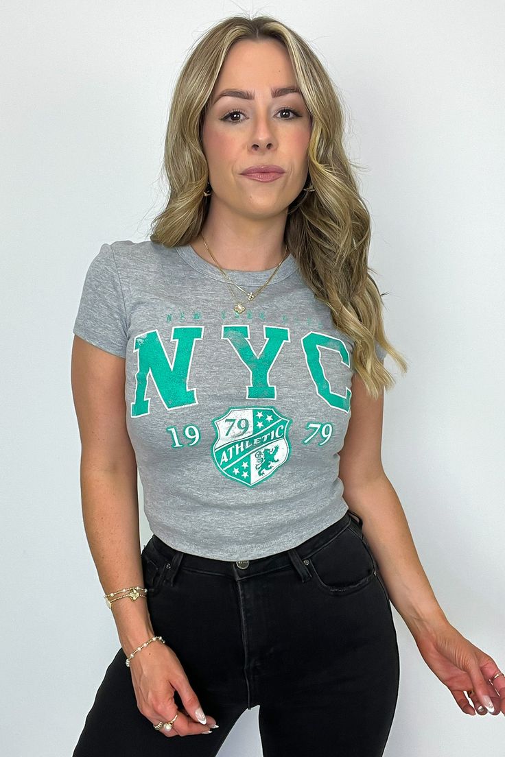 Details: Add some athletic flair to your wardrobe with our NYC Athletic Graphic Tee. With a short sleeve, fitted design and micro-ribbed fabric, this cropped tee is both comfortable and stylish. Perfect for any workout or casual day out in the city. - "NYC Athletic" graphic - Short sleeves Content: 90% COTTON 10% POLYESTER Size + Fit Model is 5'4" and wearing a Small Measurements from a size Small are approx. - Full length: 18" - Chest: 30" - Waist: 28" - Sleeves: 5" Brand: Sweet Claire Casual Cropped Crew Neck T-shirt For Workout, Sporty Stretch Cropped T-shirt With Graphic Print, Sporty Letter Print Crop Top T-shirt, Fitted Letter Print T-shirt For Athleisure, Basic Crew Neck Sports Crop Top, Sports Letter Print Crop Top T-shirt, Basic Crew Neck Crop Top For Sports, Stretch Sports T-shirt With Text Print, Sporty Short Sleeve Cropped T-shirt For Spring