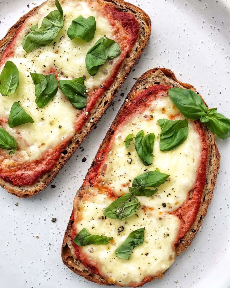 two slices of bread with cheese and basil on top, sitting on a white plate