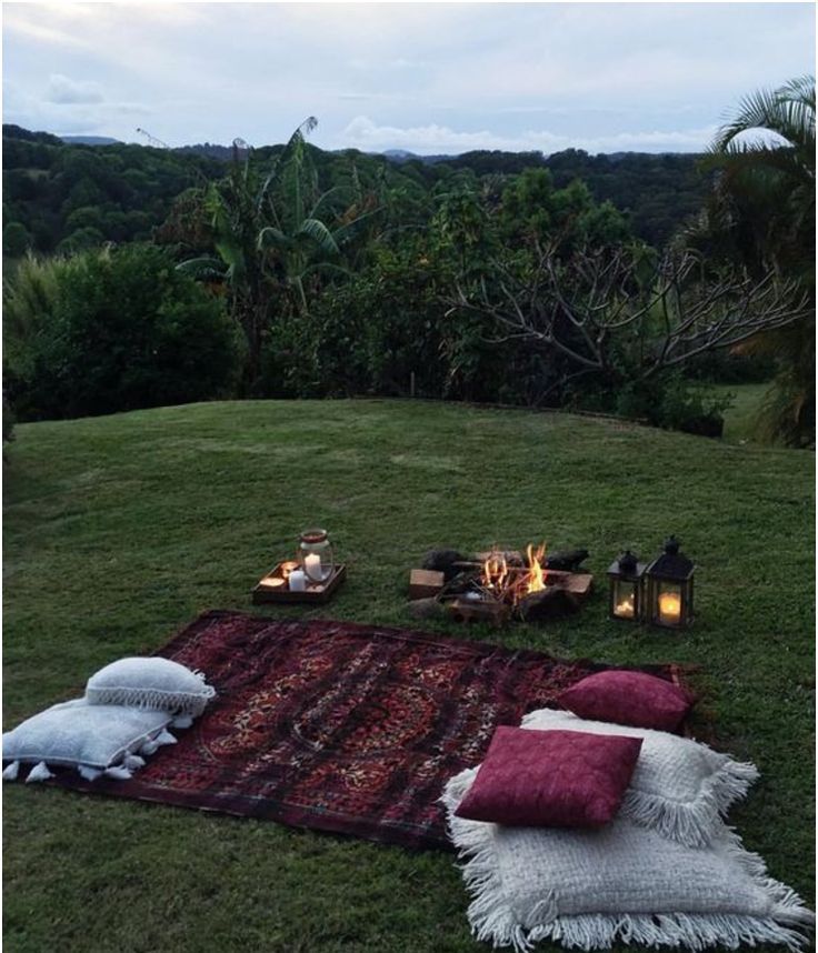 a blanket and pillows on the ground in front of a fire pit with candles lit