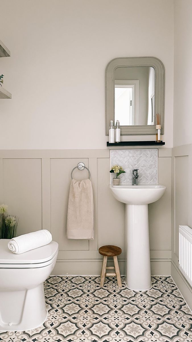 a white toilet sitting next to a sink in a bathroom under a mirror and a wooden stool