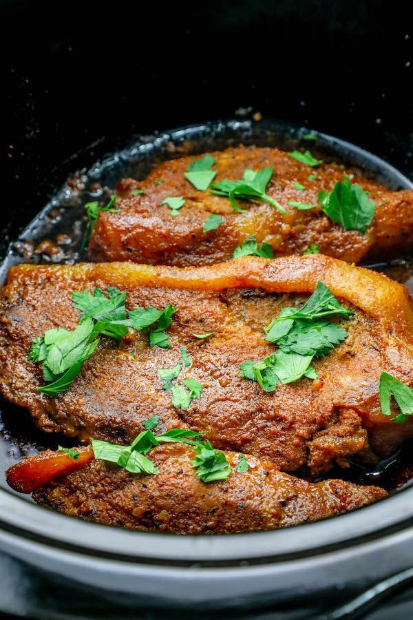 two pieces of meat in a slow cooker with herbs and spices on the side