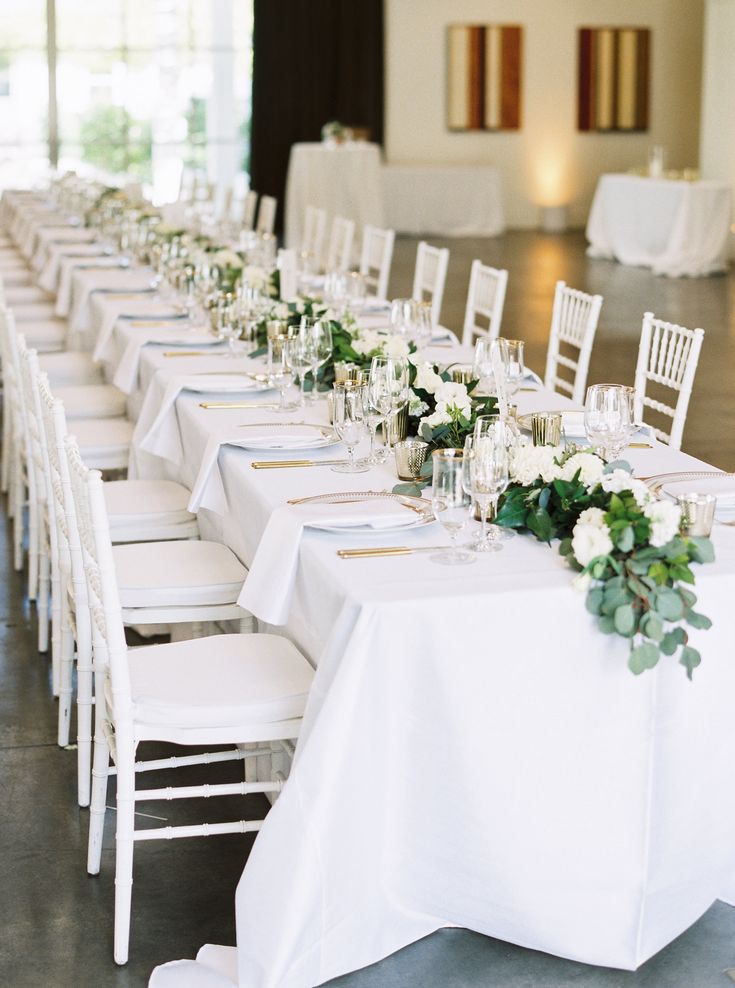 a long table with white chairs and flowers on it is set up for an event