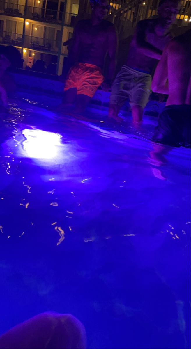 people are standing around in the pool at night