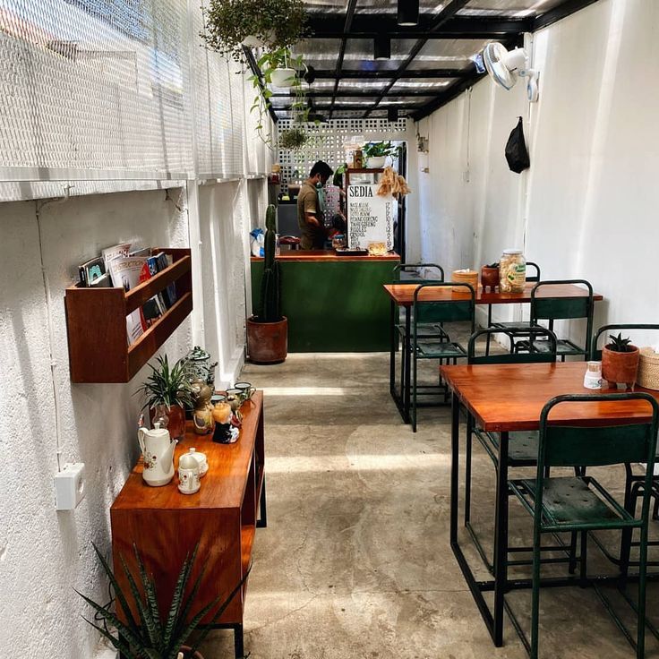 an empty restaurant with wooden tables and green chairs on either side of the table are potted plants