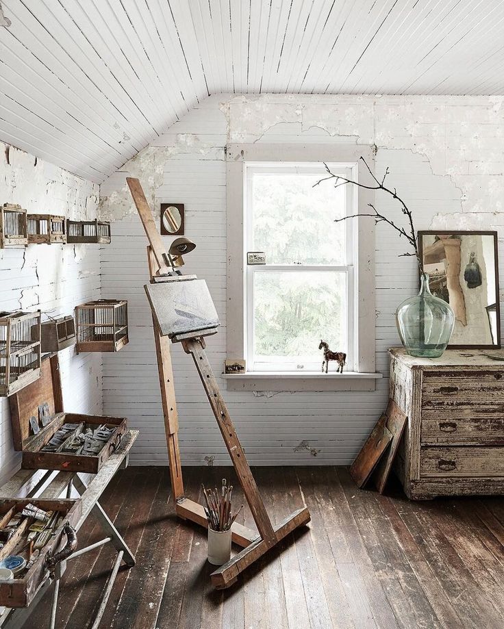 a room with white walls and wooden floors has an easel in front of the window