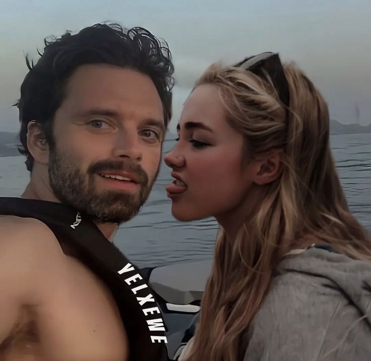 a man and woman standing next to each other in front of a body of water